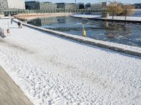 the man is walking along a frozen river bank with an empty bench and a fire hydrant