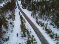 a car traveling on a snowy road through some woods from above with trees all around