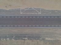 an aerial view shows the roadway with a few lines going through it, on top of a sandy desert plain