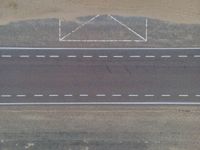 an aerial view shows the roadway with a few lines going through it, on top of a sandy desert plain