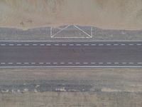 an aerial view shows the roadway with a few lines going through it, on top of a sandy desert plain