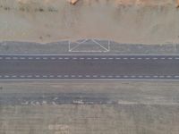 an aerial view shows the roadway with a few lines going through it, on top of a sandy desert plain