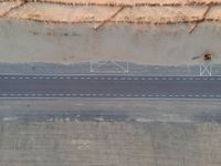 an aerial view shows the roadway with a few lines going through it, on top of a sandy desert plain