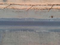 an aerial view shows the roadway with a few lines going through it, on top of a sandy desert plain