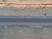 an aerial view shows the roadway with a few lines going through it, on top of a sandy desert plain