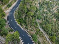 two cars traveling down an empty, winding, wide road between cliffs and trees and green vegetation