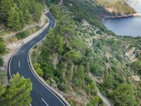 two cars traveling down an empty, winding, wide road between cliffs and trees and green vegetation