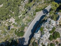 a car driving along the top of a steep mountain next to the ocean with a shadow of a car on it