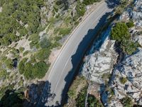 a car driving along the top of a steep mountain next to the ocean with a shadow of a car on it