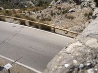 a person riding a skateboard on a long road by rocks and a cliff next to a road