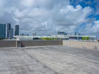 an empty parking lot that has graffiti and clouds in the sky above it and several buildings behind