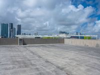 an empty parking lot that has graffiti and clouds in the sky above it and several buildings behind