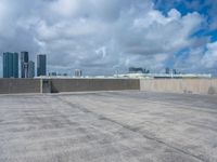 an empty parking lot that has graffiti and clouds in the sky above it and several buildings behind