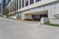 a sidewalk with an entrance to a car park and a building that has graffiti all over the side