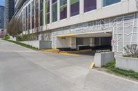 a sidewalk with an entrance to a car park and a building that has graffiti all over the side