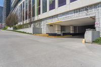 a sidewalk with an entrance to a car park and a building that has graffiti all over the side