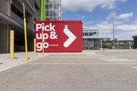 red and white sign for pick up and go parked in a parking lot next to a building