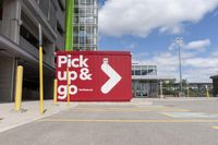 red and white sign for pick up and go parked in a parking lot next to a building