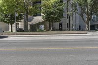 an empty street with the curb painted white in front of a tall building and some trees