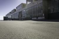 a skateboard parked in an empty parking lot near large buildings and a sidewalk with some people walking on it