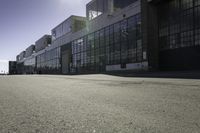 a skateboard parked in an empty parking lot near large buildings and a sidewalk with some people walking on it