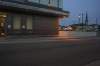 a view of the entrance of a small business in the evening time, from the sidewalk to the road