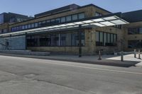 an empty street in front of an old building with many windows and a parking lot under a covering over