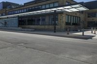 an empty street in front of an old building with many windows and a parking lot under a covering over