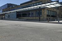 an empty street in front of an old building with many windows and a parking lot under a covering over