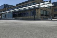 an empty street in front of an old building with many windows and a parking lot under a covering over