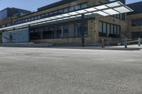 an empty street in front of an old building with many windows and a parking lot under a covering over