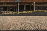 a person sitting in front of the food hall on a brick ground with an open umbrella over them