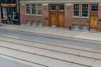 an open door to an old brick building with railroad tracks below it and steps going up the left side of the street