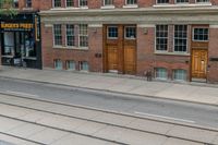 an open door to an old brick building with railroad tracks below it and steps going up the left side of the street