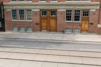 an open door to an old brick building with railroad tracks below it and steps going up the left side of the street