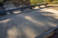 a concrete walkway leading to a river and two benches in the shade of trees next to it