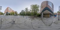 the panorama of a view through the lens of a parking lot with a building and trees in the background