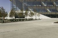 a skateboarder leaning against an asphalt parking lot near a tall glass building and trees