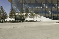 a skateboarder leaning against an asphalt parking lot near a tall glass building and trees