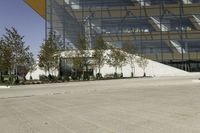 a skateboarder leaning against an asphalt parking lot near a tall glass building and trees