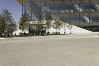 a skateboarder leaning against an asphalt parking lot near a tall glass building and trees