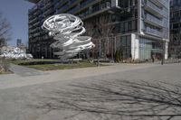 the sculpture has several white strips of fabric attached to it, by some trees and a walkway