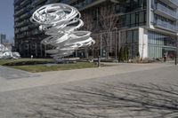 the sculpture has several white strips of fabric attached to it, by some trees and a walkway