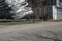 the sculpture has several white strips of fabric attached to it, by some trees and a walkway