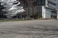 the sculpture has several white strips of fabric attached to it, by some trees and a walkway