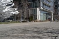 the sculpture has several white strips of fabric attached to it, by some trees and a walkway