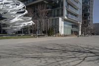 the sculpture has several white strips of fabric attached to it, by some trees and a walkway