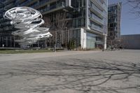 the sculpture has several white strips of fabric attached to it, by some trees and a walkway