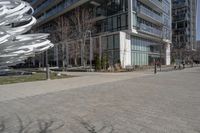 the sculpture has several white strips of fabric attached to it, by some trees and a walkway