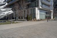 the sculpture has several white strips of fabric attached to it, by some trees and a walkway